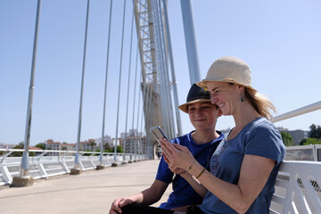 Cheerful mother and son using smartphone on bridge