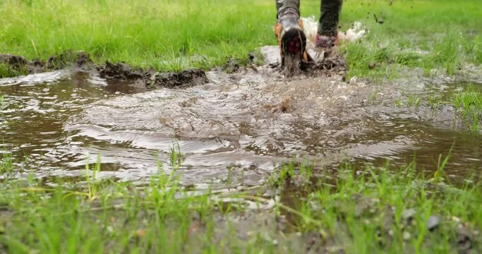 Close-up shot of a hiking boots of an outdoor man who steps into a muddy puddle and that step makes mud splashing