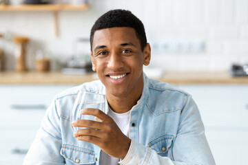 Healthy lifestyle concept. Young man holding glass of fresh clean water looks at camera, smiles...