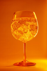 large glass with sparkling cocktail on orange background