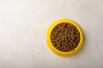 Dry cat food in a yellow bowl on a cement background. Vitamins and nutrients for good health and energy of pets.Copy space.