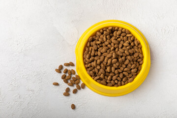 Fototapeta na wymiar Dry cat food in a yellow bowl on a cement background. Vitamins and nutrients for good health and energy of pets.Copy space.