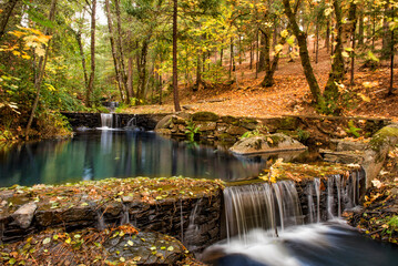 Naklejka na ściany i meble Autumn forest with waterfall. Colorful landscape with yellow and orange trees, stones and waterfall.