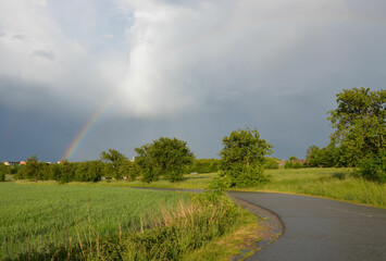 Regenbogen in Frühlingslandschaft mit Sonne und Regenwolken  