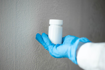 A nurse wearing blue medical gloves holds a bottle of pills