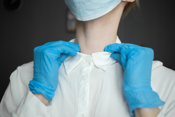 A nurse wearing a mask and protective gloves adjusts the collar of her gown
