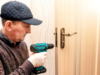 A master with an electric screwdriver repairs the door lock