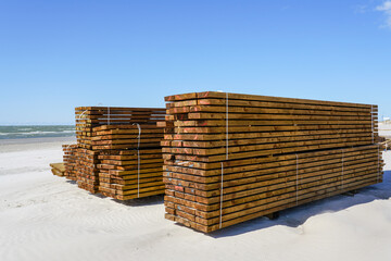 Large stacks of impregnated brown pine wood boards by the sea on a sandy beach