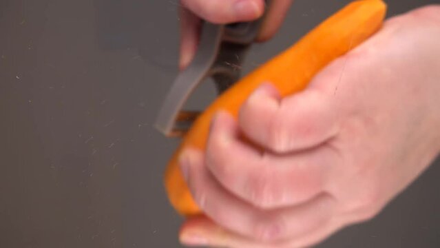 Slicing fresh carrots over a glass bowl. Bottom view.