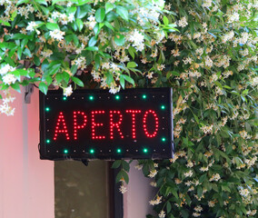 Panel with led and the text APERTO that means OPEN in Italian language and jasmine flowers