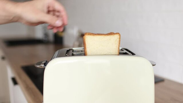 close up of hand are puting toasts bread in toaster in the kitchen. Includes kitchen appliance for making croutons and toasts for breakfast. A man's hand shoves a slice of bread into a toaster.