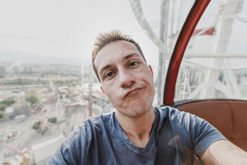 Depressed and disappointed young man taking selfie while riding ferris wheel in amusement luna...