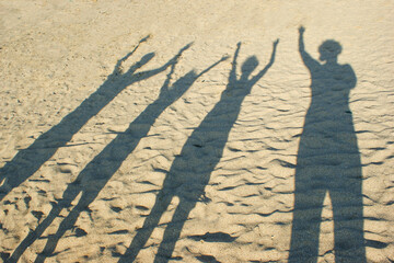  Shadow on the sand from the family, parents and children, hands raised up. Happy young family. The...