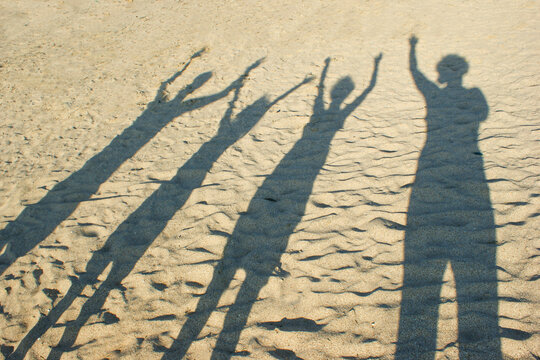  Shadow on the sand from the family, parents and children, hands raised up. Happy young family. The concept of light and shadow, happiness, vacation, travel, family values, love.