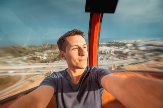 Happy and excited young man taking selfie photo in cabin of a ferris wheel. Solo travel adventures and amusement or luna park