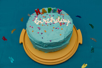 Blue iced happy birthday cake on a platter on a blue tablecloth