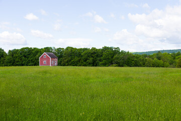 Obraz premium Pretty landscape along route 247 with small derelict red cabin in the middle of a green field in spring, Stanstead, Quebec, Canada