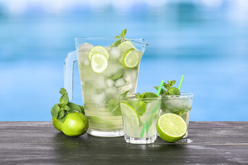 Glasses and jug of cold mojito cocktail on edge of swimming pool