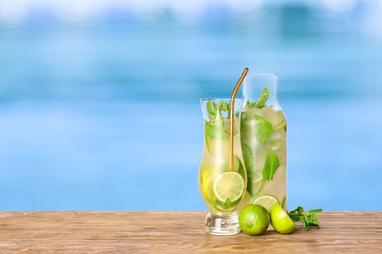 Glass and bottle of cold mojito cocktail on edge of swimming pool