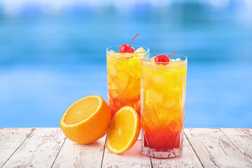 Glasses of cold Tequila Sunrise cocktail on edge of swimming pool