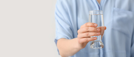 Woman holding glass of water on light background, closeup