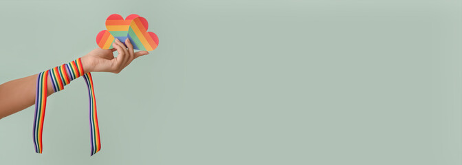 Female hand with rainbow hearts and ribbon on color background with space for text. LGBT concept