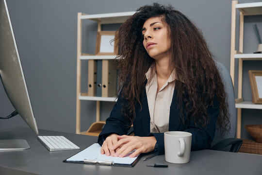 Tired Bored Sleepy Tanned Adorable Curly Latin Businesswoman In Jacket Have Too Much Work Looks At Monitor In Office. Copy Space Mockup Banner. Corporation Leader Lady Uses Modern Computer In Work