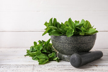 Mortar and pestle with mint leaves on light wooden background