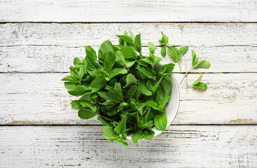 Bowl with mint leaves on light wooden background