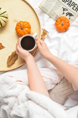 Woman drinking tasty pumpkin coffee on bed