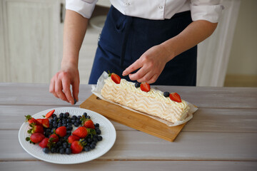 The chef decorates the dessert cake with fresh berries: strawberries and blueberries in the kitchen