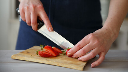 The hands of the cook cutting fresh strawberries in the kitchen for cooking