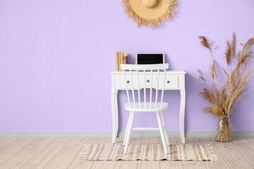 Stylish workplace with modern laptop and vase with reed flowers near violet wall in room interior