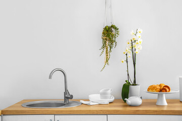 Beautiful orchid flower, dishware and sink on kitchen counter near white wall