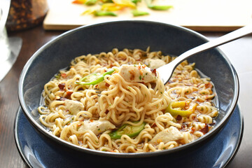 Instant noodles on fork.  Spicy chicken noodles soup in a bowl. 