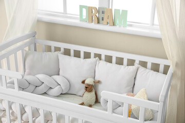 Baby crib with pillows and toy near window