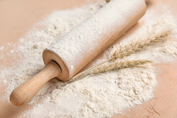 Rolling pin and wheat flour on color background, closeup