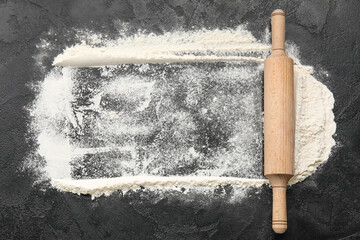 Frame made of flour and wooden rolling pin on dark background