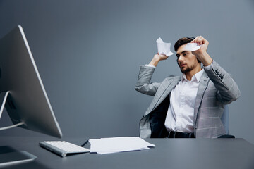 handsome man in headphones in a gray suit sits in front of a computer Gray background