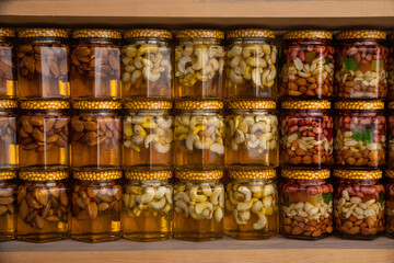 Various nuts in honey. A stand with products in the street market. Cashews, walnuts, almonds, hazelnuts and other nuts in honey or syrup in jars. Selective focus