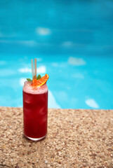 Fresh alcoholic red summer cocktail with ice on edge of pool in the hotel recreation area. Selective focus
