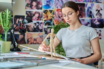 Teenage creative girl artist drawing with a pencil, sitting at the table at home