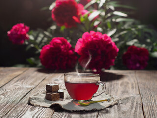 A cup of red hot steaming tea standing on a napkin and a textured table with waffle sweets in low...