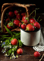 Wild strawberries in an enameled cup and a bouquet of wildflowers, close-up, low key