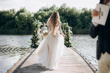 Foto op Plexiglas the bride goes to meet the groom at the wedding ceremony on the pier by the lake © Юлия Чернецкая