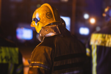 Obraz premium Group of fire men in uniform during fire fighting operation in the night city streets, firefighters with the fire engine truck fighting vehicle in the background, emergency and rescue