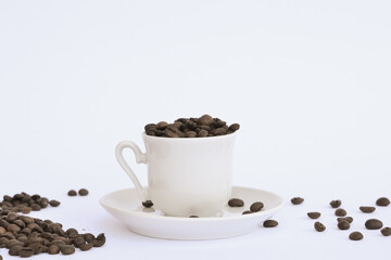 Coffee beans are spread around a white cup and saucer on a white background