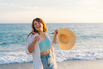 Portrait of a happy young girl in a straw hat with a cocktail in hand on a background of beautiful...