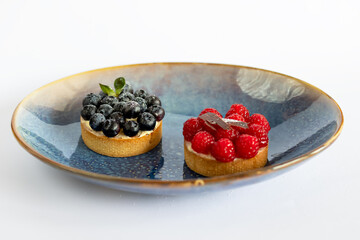 Dessert with fresh berries sprinkled with powdered sugar on a blue plate. White background. minimalism