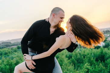 man and woman in black clothes hugging at sunset
